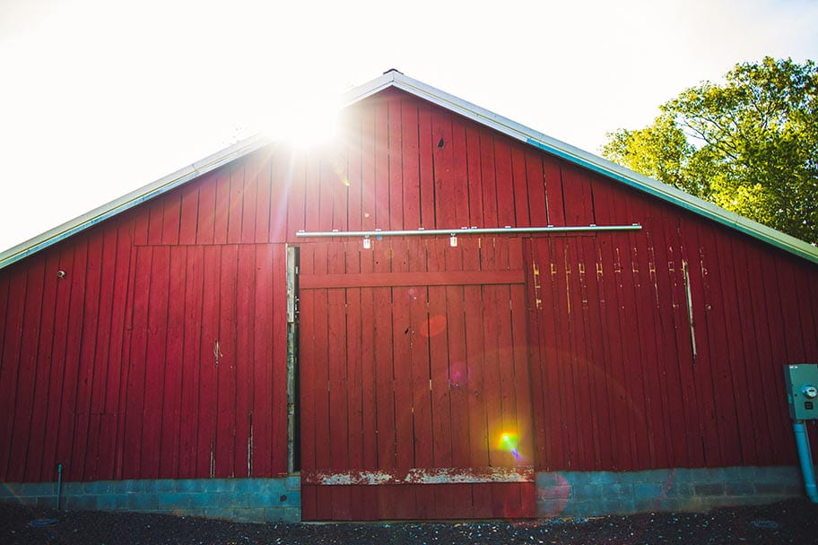 Front side of a red barn with sun behind it 